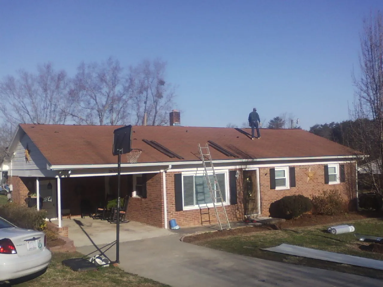 Roofer stripping a shingle roof on a brick ranch before metal panels in Raleigh