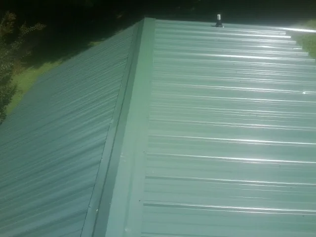 New green metal panels meeting at the ridge of a roof — Flat Roof Repair work by our crew in Raleigh
