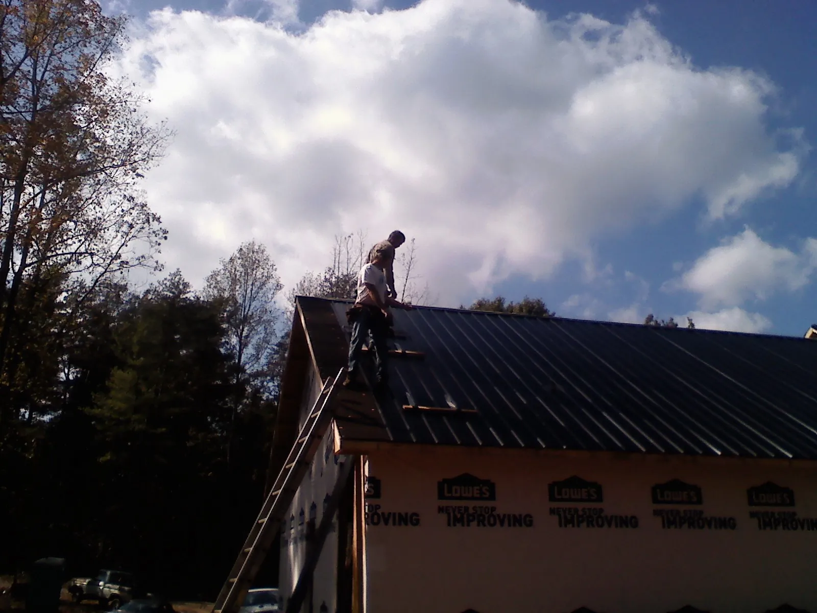 Roofer fastening dark metal panels high against a cloudy sky, from a Roof Inspection job in Raleigh